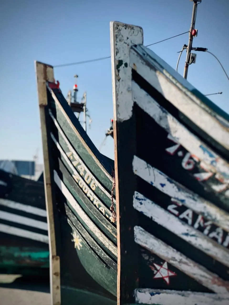 Deux proues de barques de pêche aux couleurs vives, serrées l'une contre l'autre sous un ciel bleu.