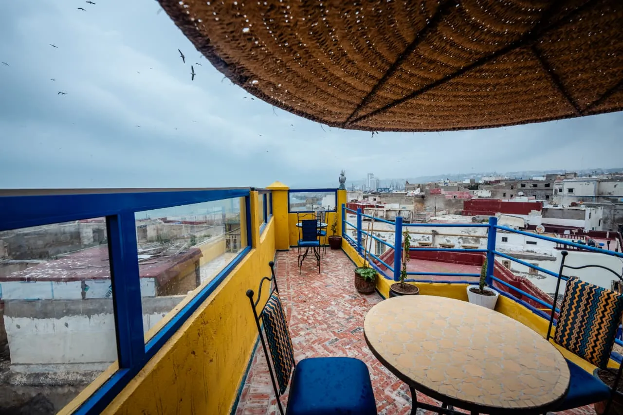 Terrasse sur le toit du Riad Bleu Azahraa avec table et vue sur la ville et l'océan.